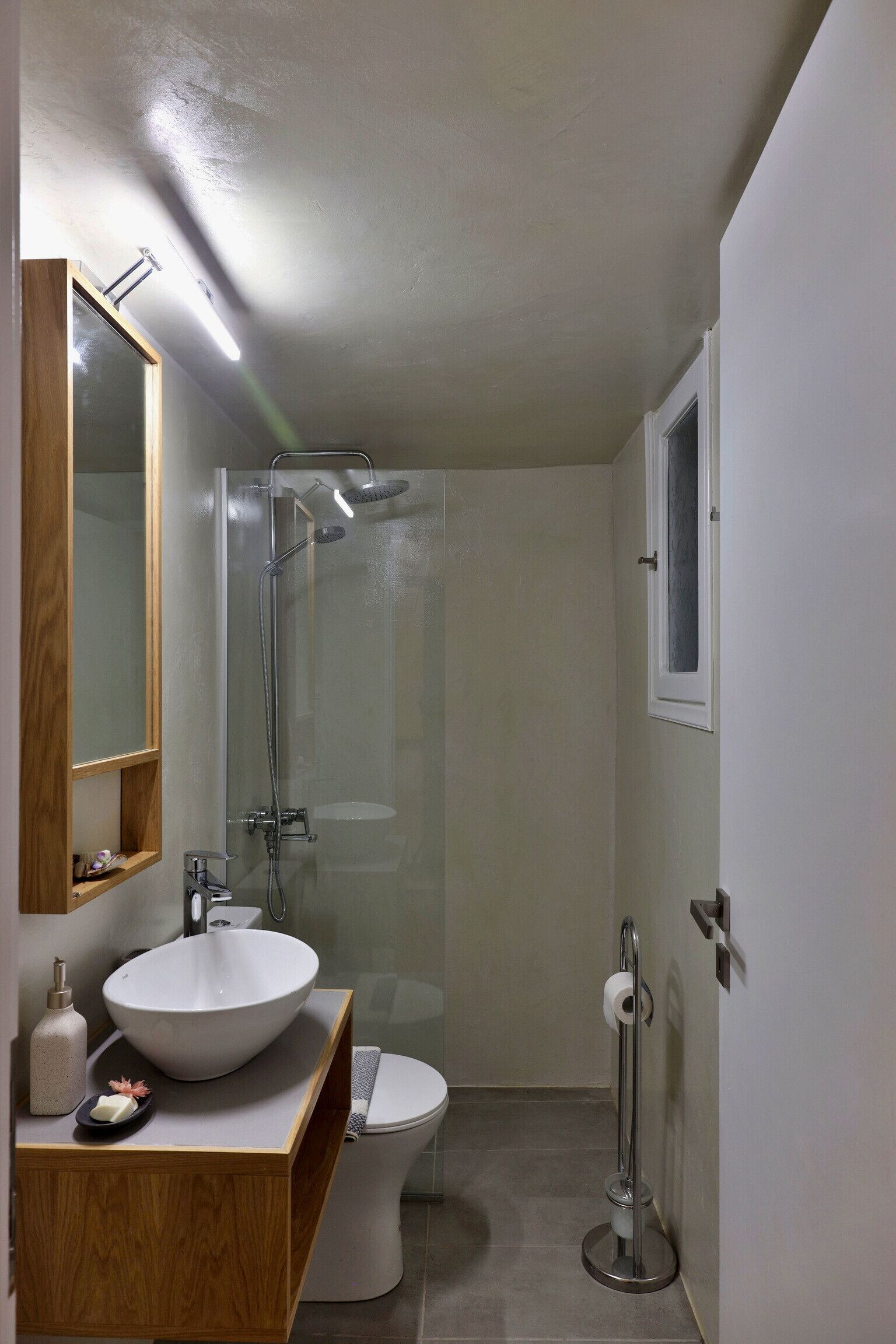 Ein modernes Badezimmer mit einer Duschkabine aus Glas, einem weißen Waschbecken, einer Toilette und einem hölzernen Waschtisch.