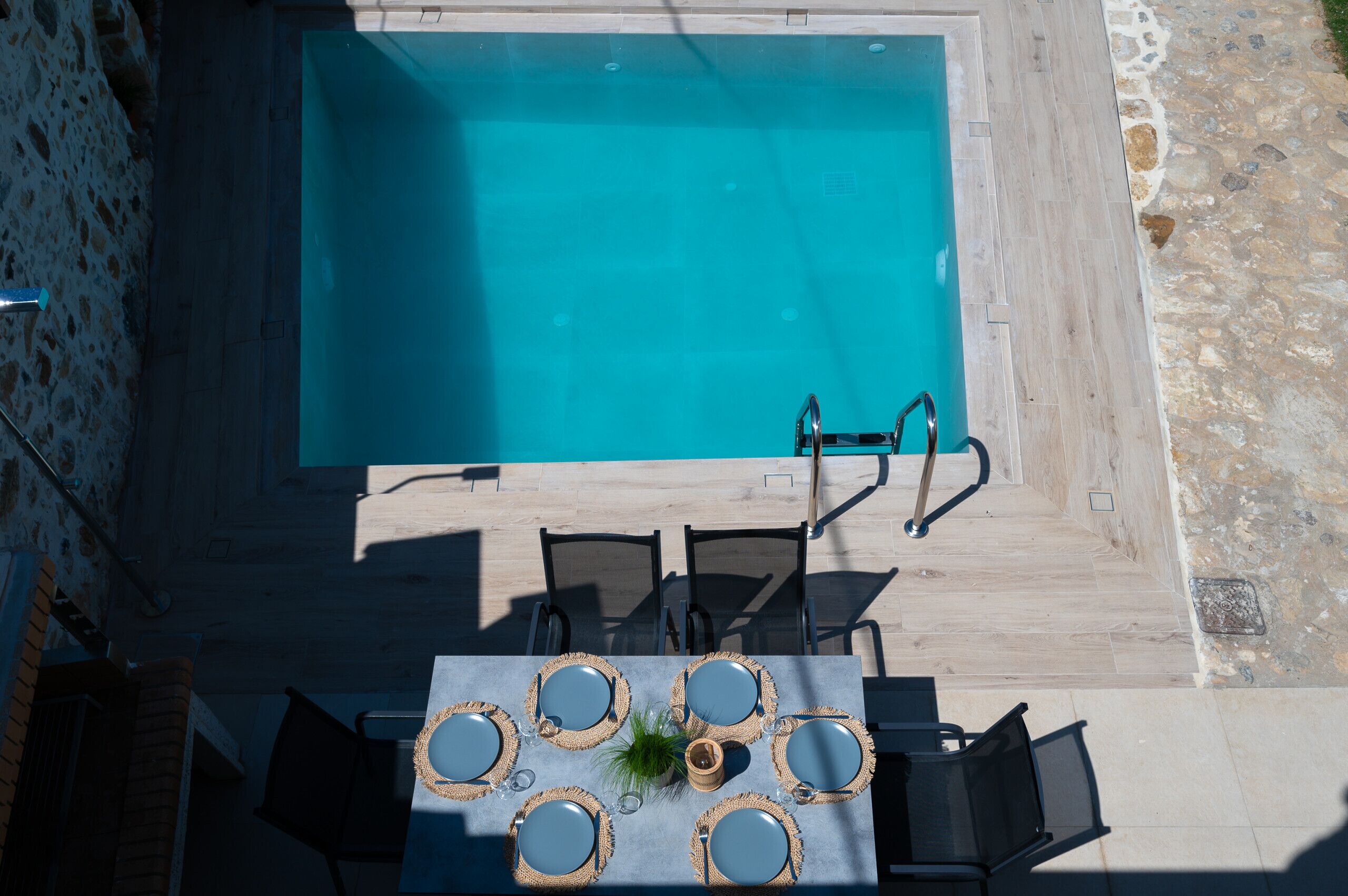 An outdoor swimming pool with a table set for six, surrounded by chairs, and a stone pathway.