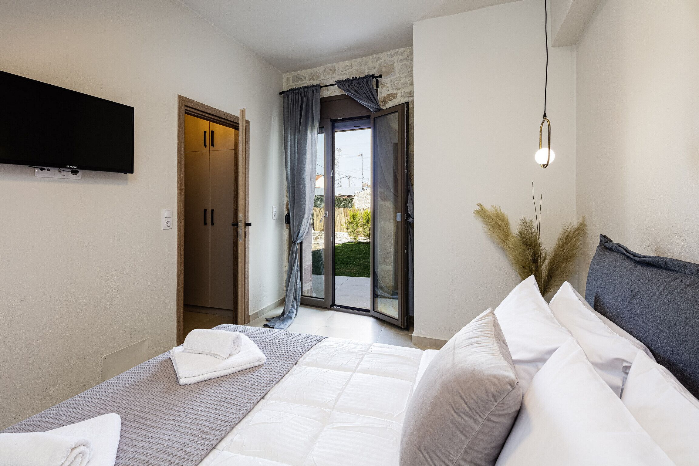 Ein Schlafzimmer mit Bett, Fernseher, einer Schiebetür und einer Wandleuchte.