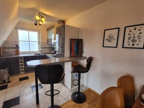 A modern kitchen with a bar area, two bar stools, and a view of the sea through a window. - Vue sur Vilm Apartment - quiet apartment with a view of the sea - (Putbus)