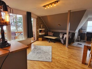 A loft-style living space with a fireplace, a sofa, a dining table, and a kitchen area. - Apartment Blick auf Vilm - quietly located apartment with sea view - (Putbus)