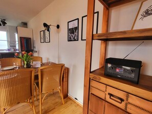 Ein Essbereich mit Korbstühlen, einem Tisch gedeckt mit Tellern und Gläsern sowie einem Radio auf einem Holzregal.