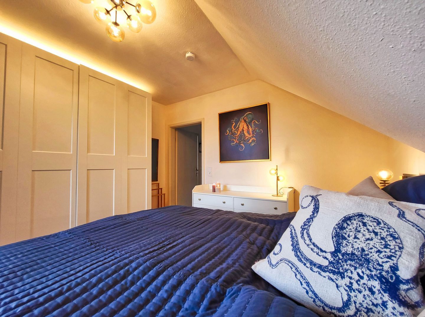A bedroom with a bed, a dresser, a painting, and a ceiling light fixture.