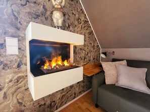 A modern living room with a built-in fireplace, a stone wall, a wooden bench, and a green sofa. - Apartment Blick auf Vilm - quietly located apartment with sea view - (Putbus)