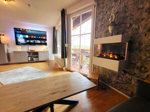 A modern living room with a flat-screen TV, a stone fireplace, and a sliding glass door leading to an outdoor area. - Apartment Blick auf Vilm - quietly located apartment with sea view - (Putbus)