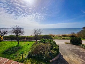 A coastal view with a paved path leading to the sea, surrounded by greenery and a clear sky. - Apartment Blick auf Vilm - quietly located apartment with sea view - (Putbus)