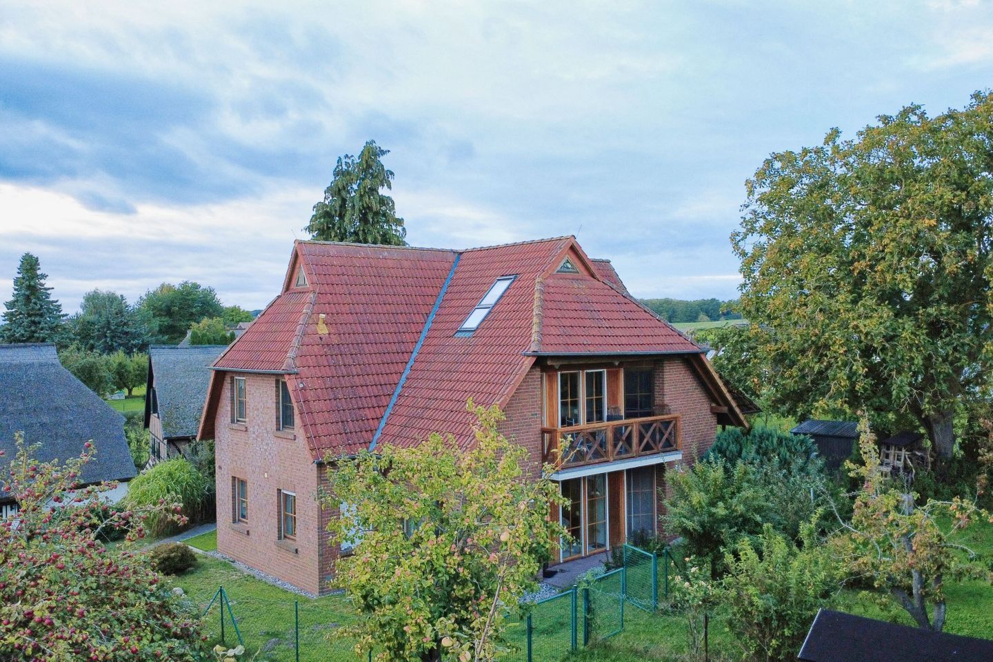 Een tweelaags huis met een rood dak, een zichtbare zolder en een balkon.