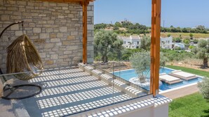 A balcony with a stone wall, a hanging chair, and a view of a swimming pool and surrounding landscape. - Thyme Villa (Rethymno)