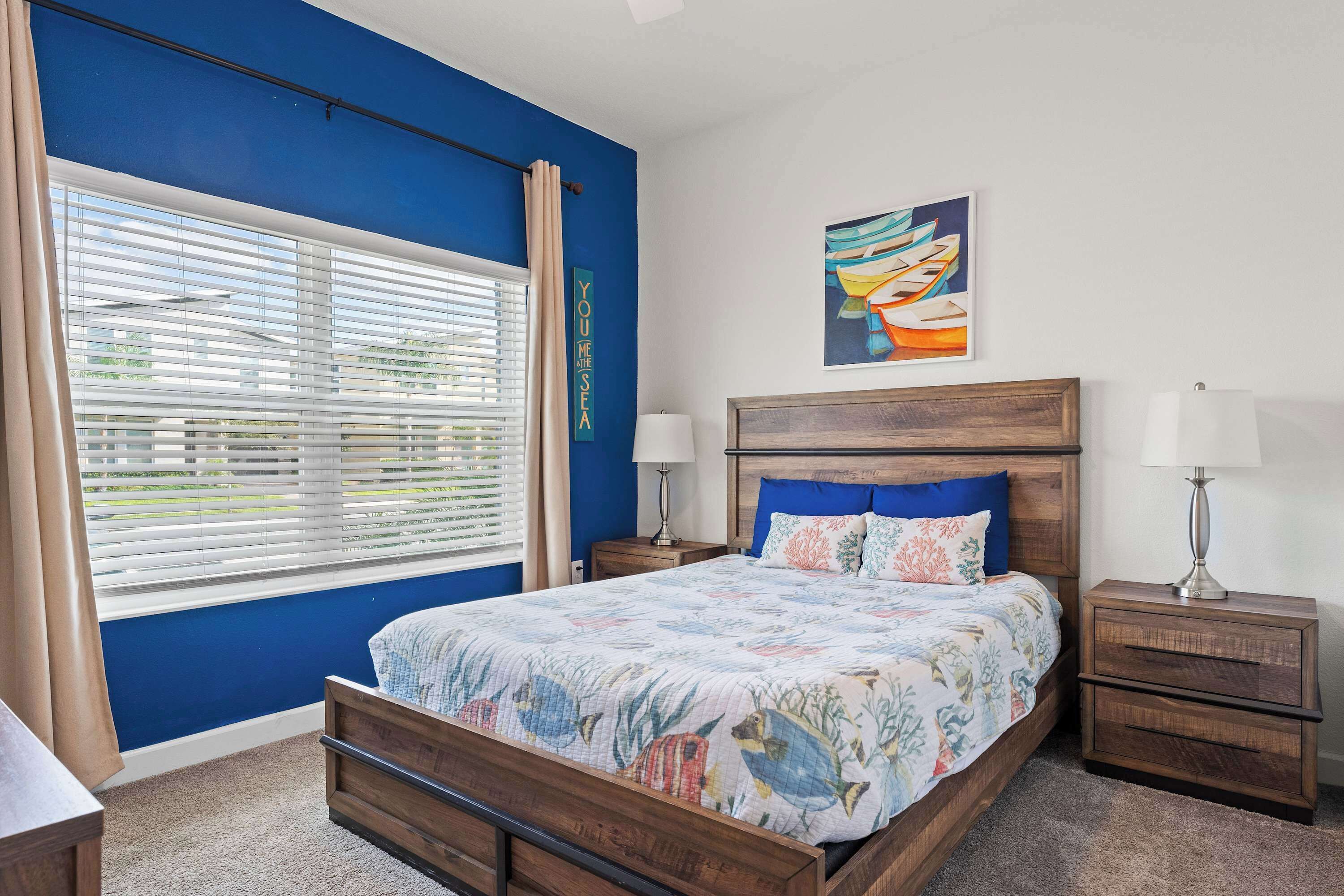 A bedroom with a bed, two nightstands, a window with blinds, and a wall with a painting.