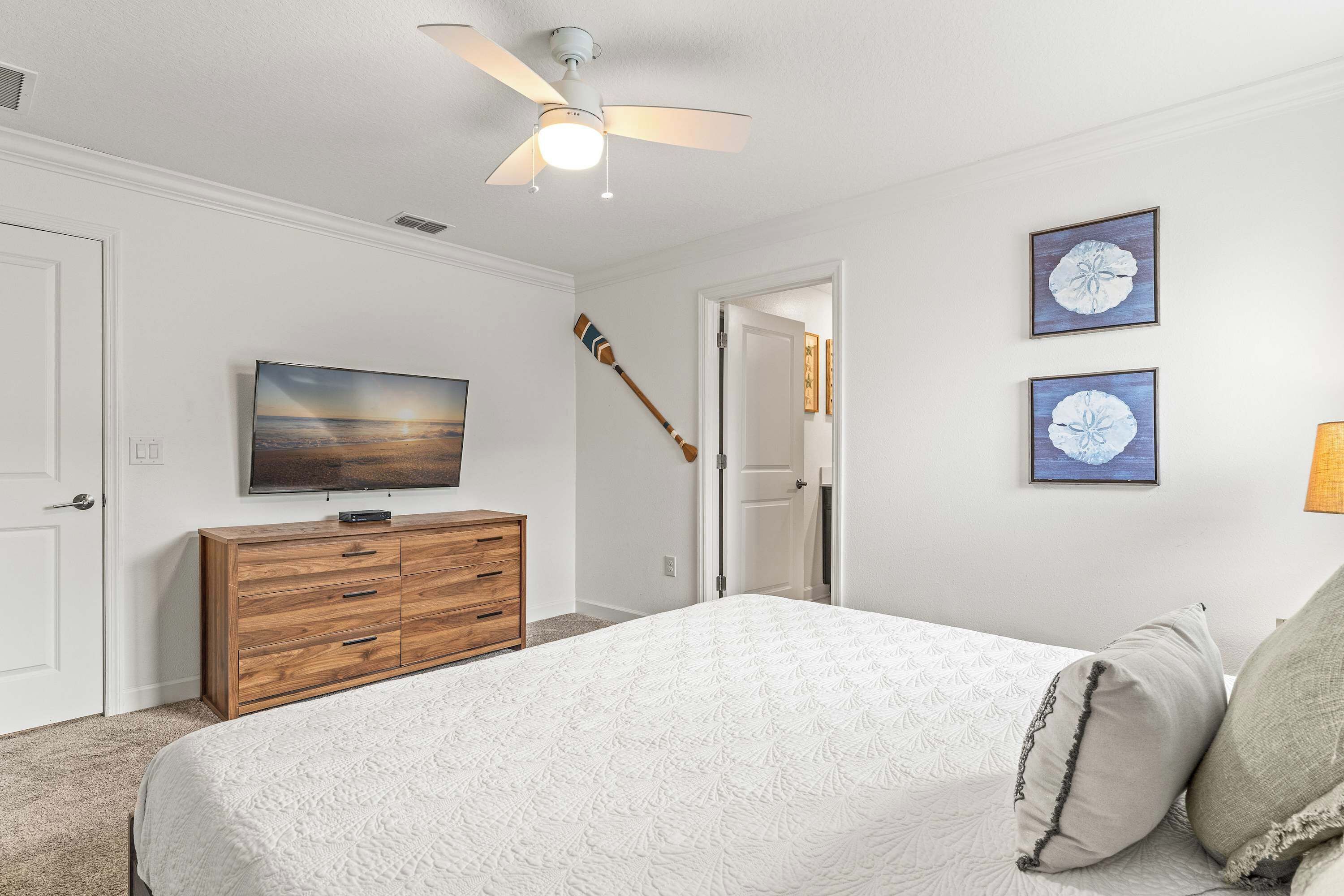 A bedroom with a bed, a wooden dresser, a ceiling fan, and two framed pictures on the wall.