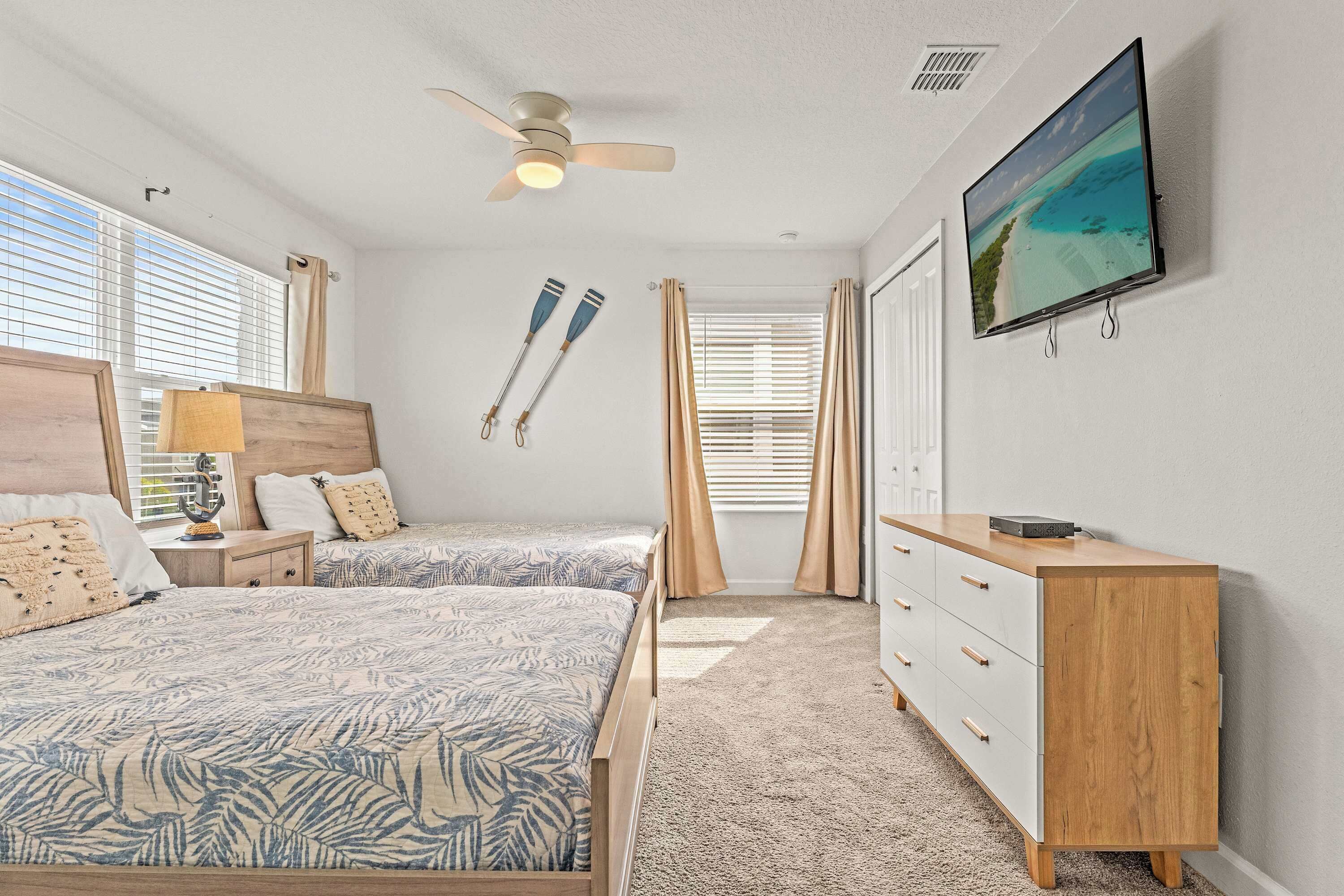 A bedroom with two beds, a ceiling fan, a TV on the wall, and a wooden dresser.
