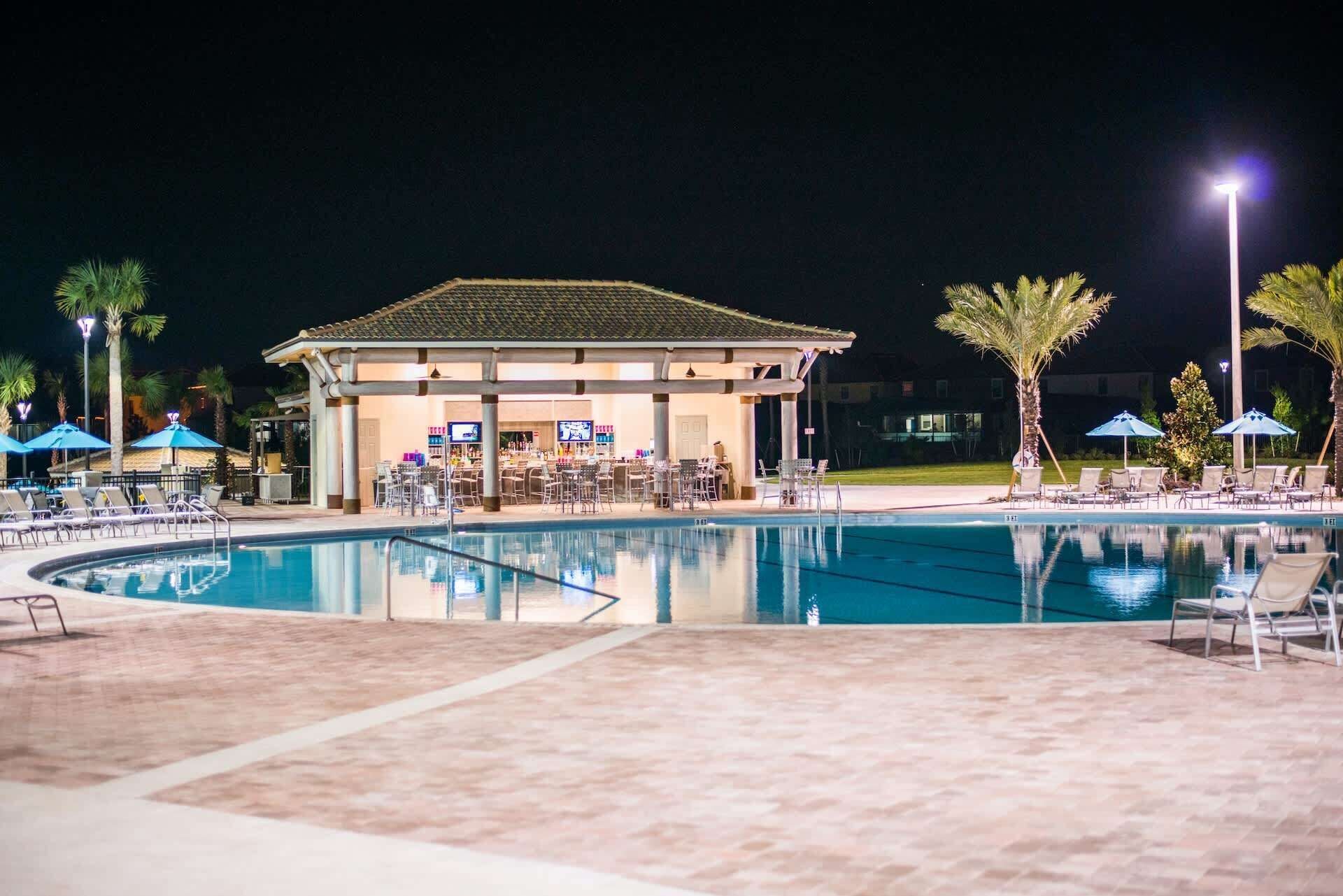 A nighttime pool area with lounge chairs, umbrellas, and a bar area.