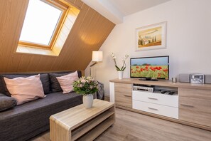 Ein modernes Wohnzimmer mit schrägverdeckter Decke, einer Couch, einem Couchtisch, einem Fernseher, einem Schrank und einem Gemälde.