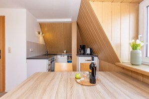 Eine moderne Küche mit Holzboden, einem Esstisch mit Flasche und Apfel, sowie einer Vase mit Blumen auf der Fensterbank.