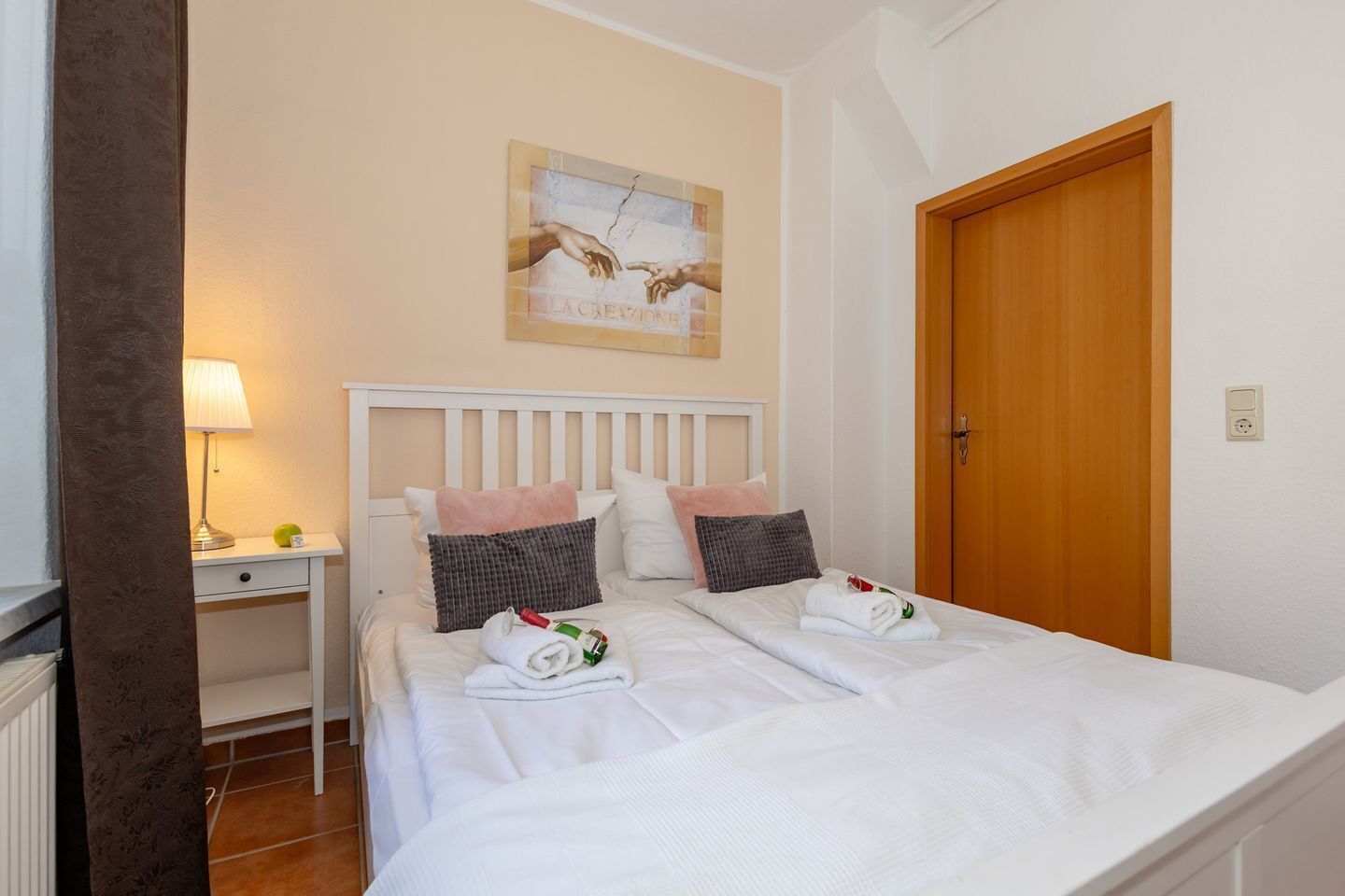 A hotel room with a bed, a nightstand, a lamp, a painting, and a wooden door.