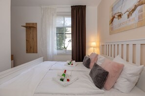 Ett hotellrum med en stor säng, ett fönster med gardiner, en tavla på väggen och en flaska champagne på sängen.