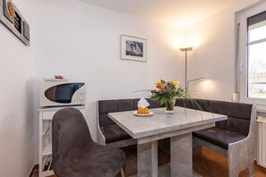 A small dining area with a table, chairs, a microwave, a vase with flowers, and a picture on the wall. - Harmonie Vacation Rental - Harmonie Vacation Apartment in Rerik - Comfortable (Rerik)