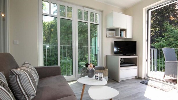 A modern living room with a sofa, a coffee table, a TV, and a balcony with a chair. - Linden Palais We 22 - Comfortable stay at the Linden Palais We 22 in (Bad Doberan)