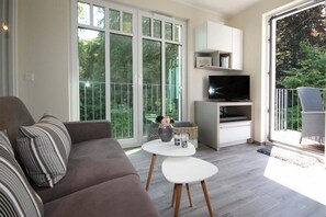 Un salon moderne avec un canapé, une table basse, un téléviseur et un balcon équipé d’une chaise.