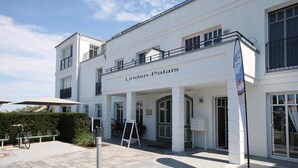 A white building with the name 'Linden-Palais' on the facade. There are outdoor umbrellas and a bicycle parked outside. - Linden Palais We 22 - Comfortable stay at the Linden Palais We 22 in (Bad Doberan)