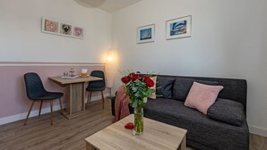 Una sala de estar acogedora con un sofá, una mesa de comedor con sillas, un florero con flores y decoración en la pared.