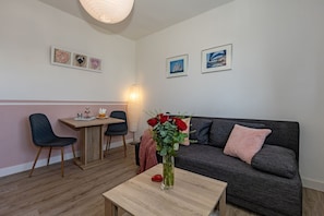 Un salon chaleureux avec un canapé, une table à manger et des chaises, un vase rempli de fleurs et des œuvres d’art accrochées au mur.