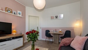 Una sala de estar con televisor, una mesa de centro con un jarrón de flores, un sofá y un comedor con sillas y una mesa.