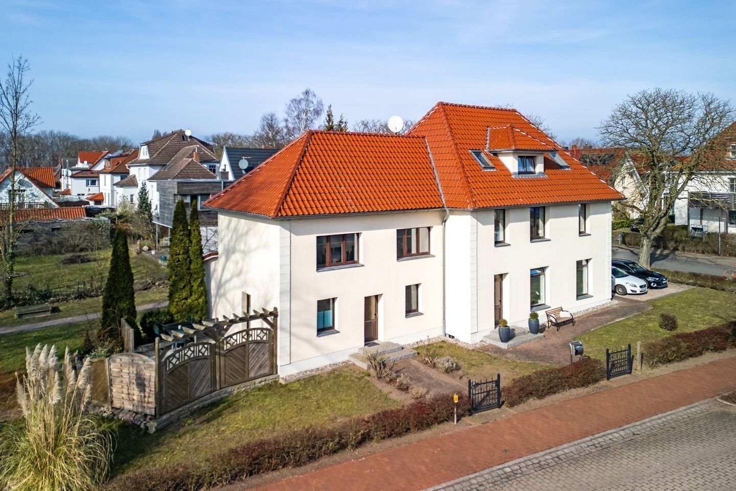 Une maison à deux étages, avec un toit recouvert de tuiles rouges, des murs extérieurs blancs et un petit porche à l’avant, équipé de sièges.