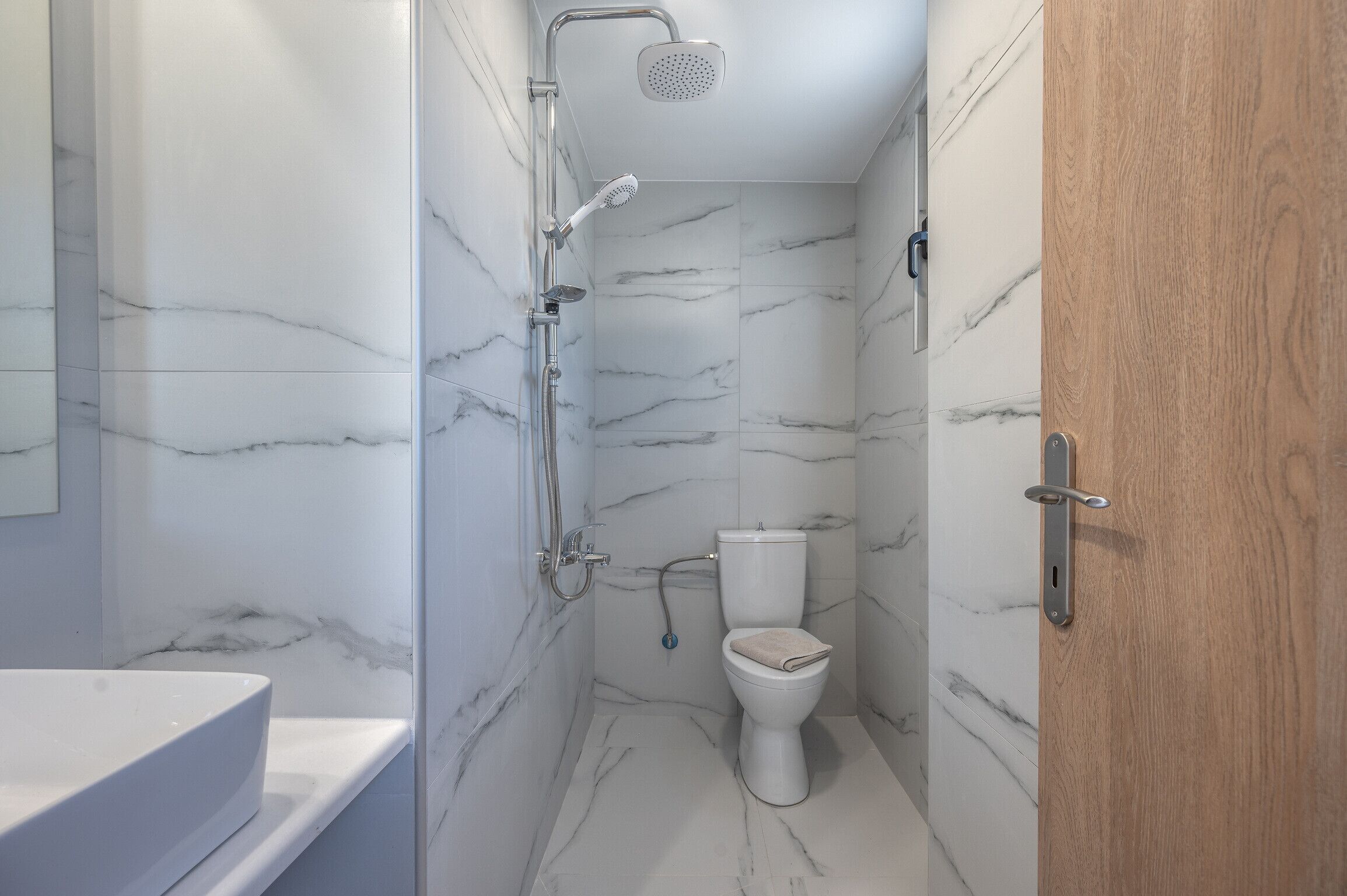 A bathroom with a white toilet, a shower with a handheld showerhead, and a marble wall.