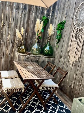 Un coin repas rustique en bois, avec une table et des chaises, décoré de plumes d’herbe des pampas dans des vases en verre et d’un attrape-rêves.
