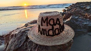 Ein gewebter Strohhut mit dem Aufdruck 'MOA Andina', platziert auf einem Felsen am Strand bei Sonnenuntergang.