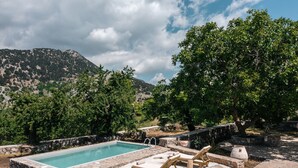 A pool area with stone walls and lounge chairs, surrounded by trees and a mountainous backdrop. - Nomas Home Imbros (Sfakia)