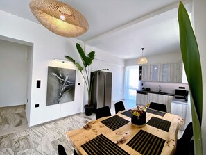 Un comedor moderno con una mesa de madera, sillas negras, una planta grande en maceta y un colgante.