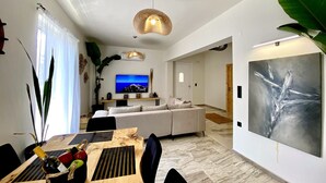 Een moderne woonkamer met een televisie, bank, eettafel en groot kunstwerk.
