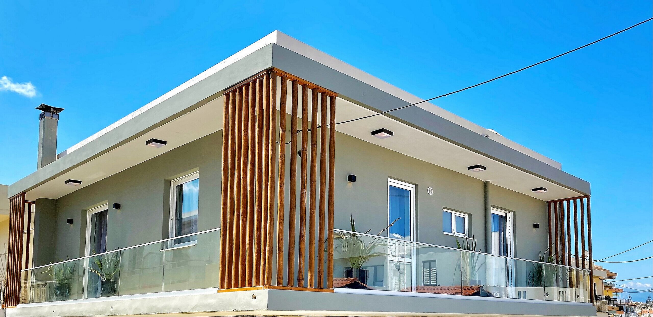 A modern two-story building with a flat roof, large windows, and a balcony with glass railings.