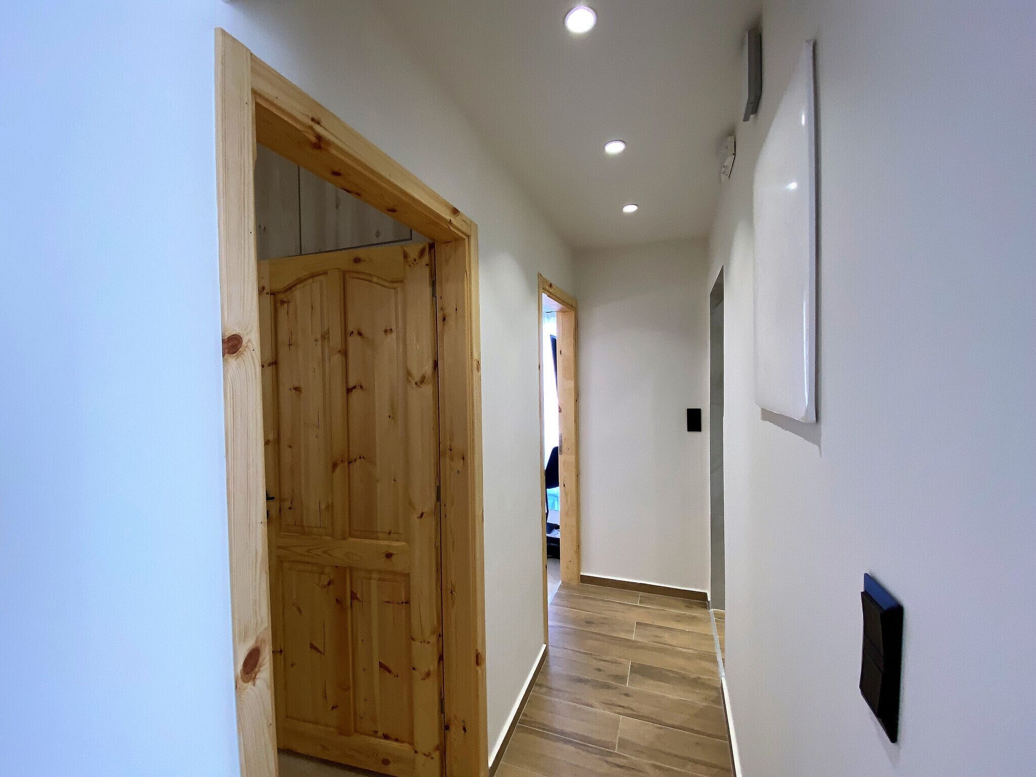 A hallway with a wooden door, white walls, and a tiled floor.