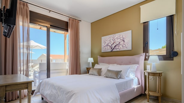 A bedroom with a large bed, a bedside table, a lamp, and a window with curtains. - Jason Panorama Villa 1 (Rethymno)