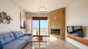 A modern living room with a sofa, a coffee table, a flat-screen TV, and a fireplace. - Jason Panorama Villa 1 (Rethymno)