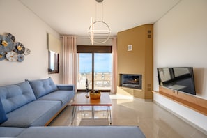 A modern living room with a sofa, a coffee table, a flat-screen TV, and a fireplace. - Jason Panorama Villa 1 (Rethymno)