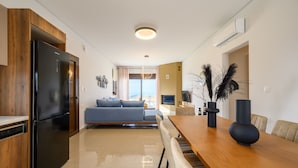 A modern kitchen with a black refrigerator, wooden cabinets, a dining table with chairs, and a view of the sea through large windows. - Jason Panorama Villa 1 (Rethymno)