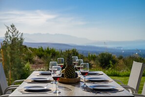 A table set for a meal with a pineapple centerpiece, wine glasses, and plates, overlooking a scenic landscape with mountains and greenery. - Jason Panorama Villa 2 (Rethymno)