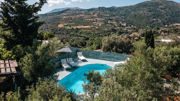 A pool area with lounge chairs and a pergola, surrounded by trees and overlooking a hilly landscape. - Rogalida Villa (Agios Vasileios)