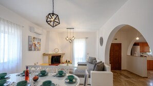 A modern living room with a dining area, white walls, and a kitchen visible through an archway. - Vigla Villa (Viannos)