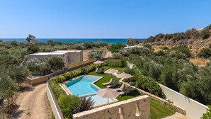 A pool area with a view of the sea, surrounded by greenery and a stone wall. - Vigla Villa (Viannos)