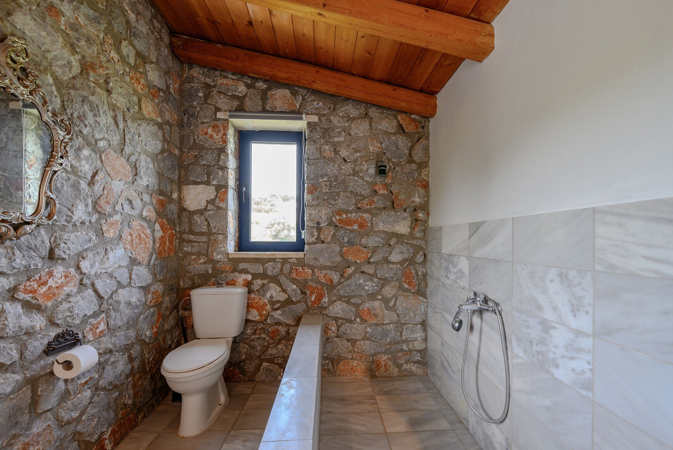 Ein Badezimmer mit Steinwand, Holzboden, Toilette, Badewanne und Dusche.