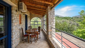 Une pièce aux murs de pierre et au plafond en bois, avec une table à manger et des chaises, et une vue sur un paysage montagneux par une grande fenêtre en arc de cercle.