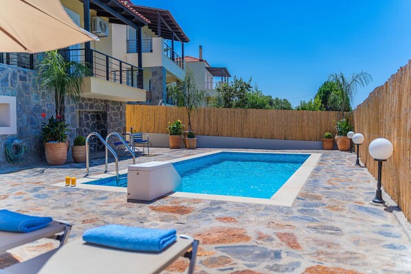 Ein Pool mit Steinböden, Liegestühlen und Kübelpflanzen.
