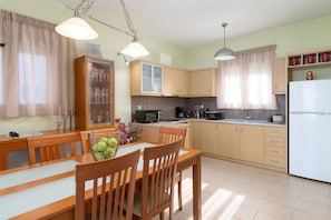 A modern kitchen with wooden cabinets, a dining table with chairs, and a refrigerator. - Papida Grande Villa (Rethymno)