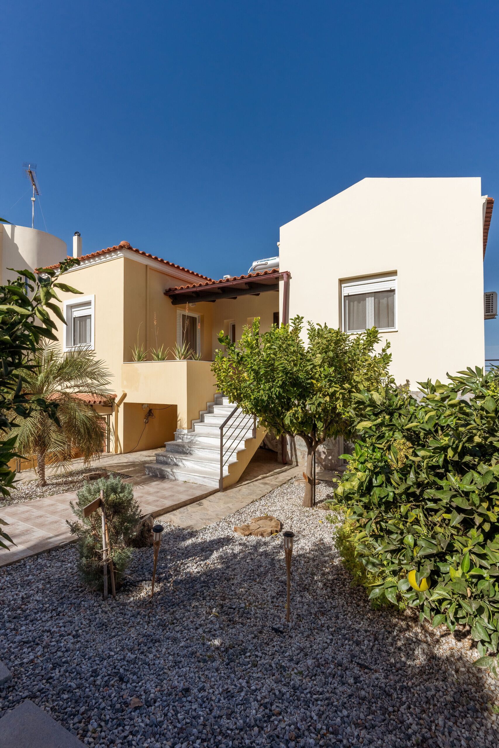A residential building with a tiled roof, a staircase leading to a balcony, and a gravel driveway.