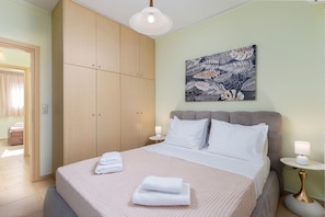A neatly arranged bedroom with a bed, a wardrobe, a nightstand, and a wall-mounted lamp. - Papida Grande Villa (Rethymno)